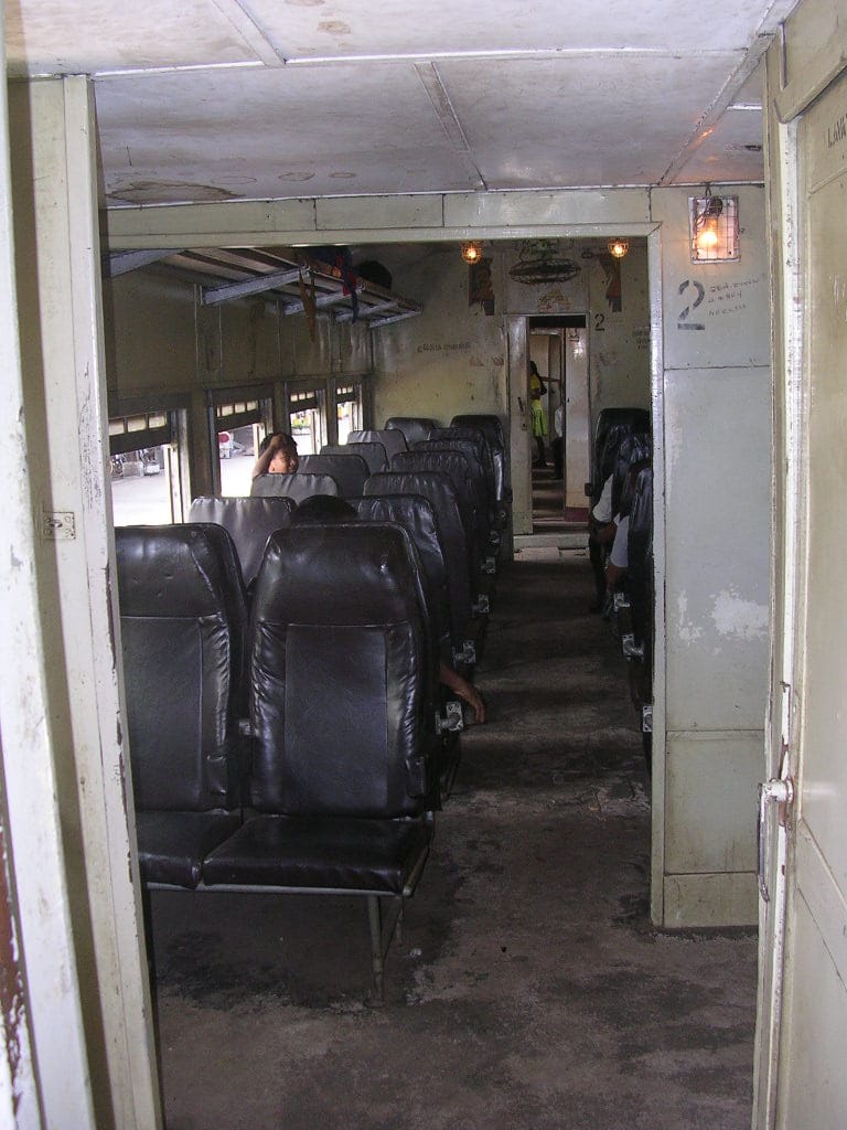 Interior of an older Sri Lanka Railways carriage with rows of black padded seats
