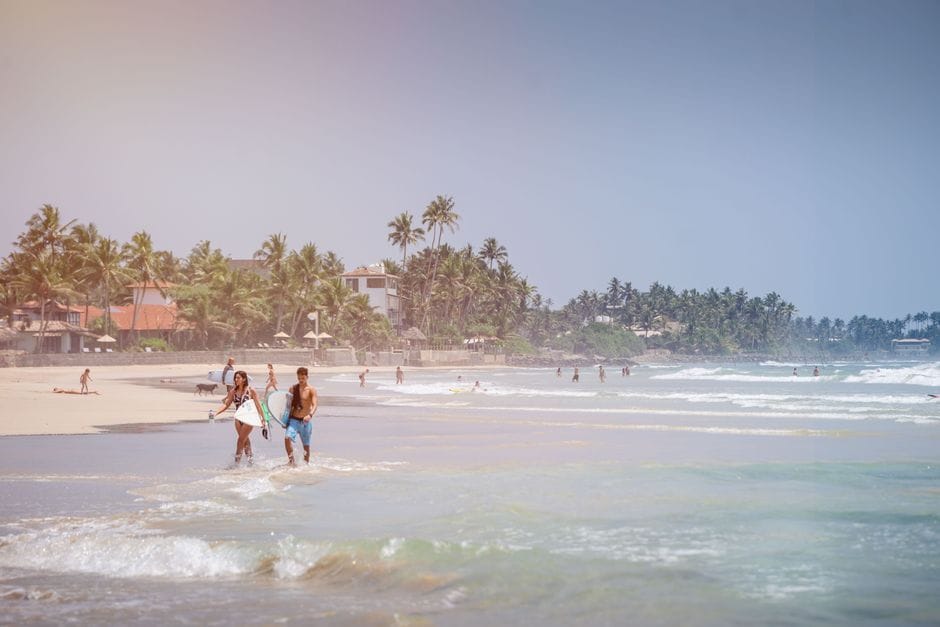 Couple carrying surfboards along a sunny beach in Sri Lanka.