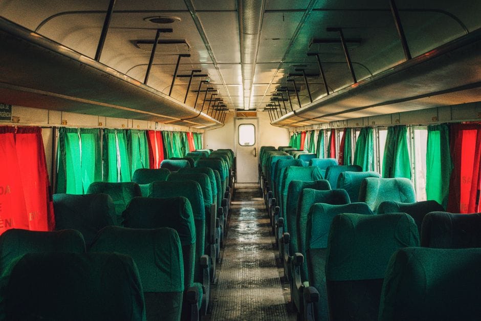 Interior of an empty train carriage with green seats and colorful curtains.