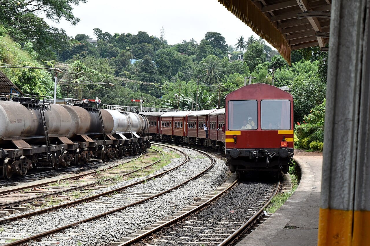 Red Sri Lanka Railways passenger train arriving at a hill-country station platform